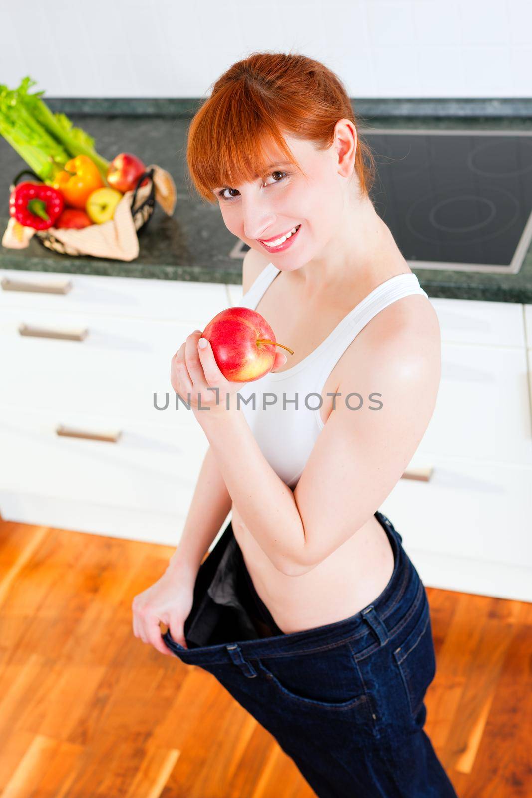 Woman trying her last year's jeans finding them way too big after she lost so much weight; she has an apple in her hand