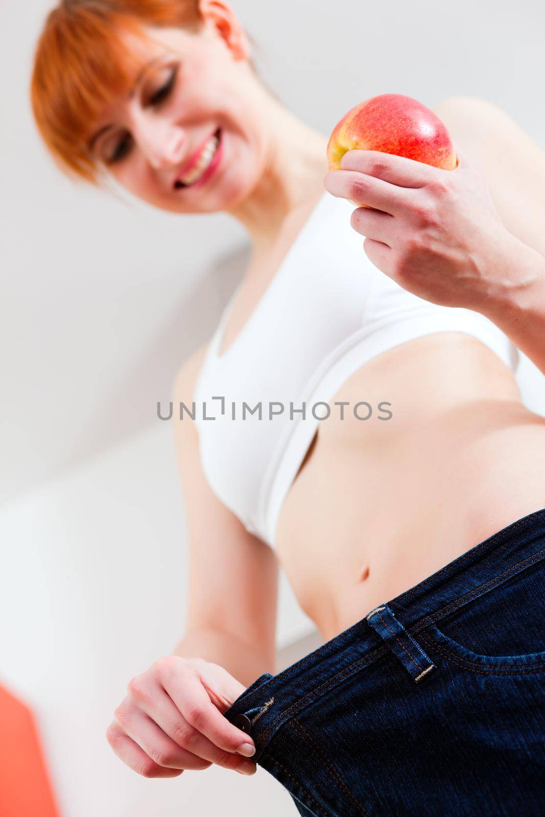 Woman trying her last year's jeans finding them way too big after she lost so much weight; she has an apple in her hand