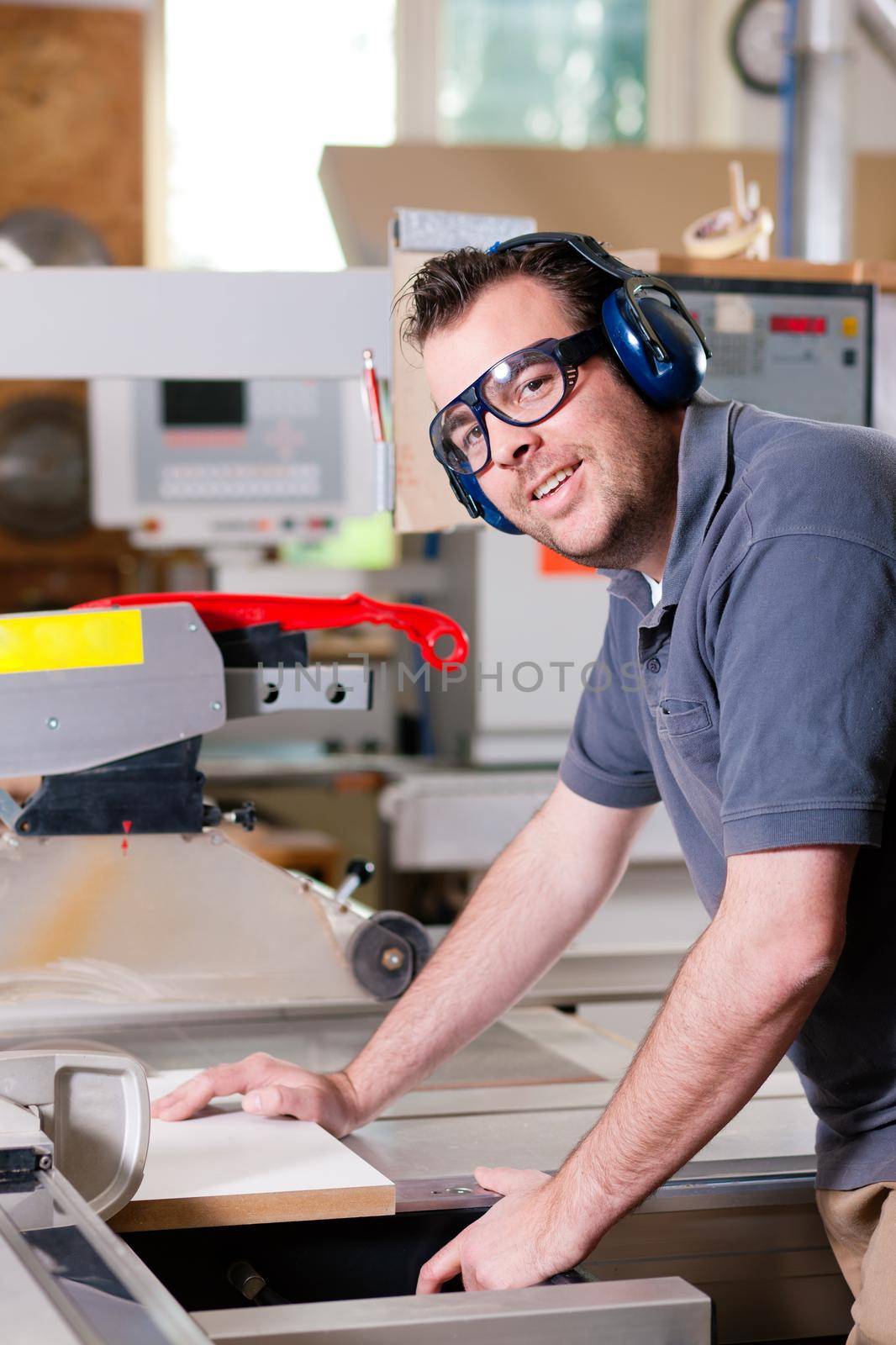 Carpenter working on an electric buzz saw cutting some boards, he is wearing safety glasses and hearing protection to make things safe