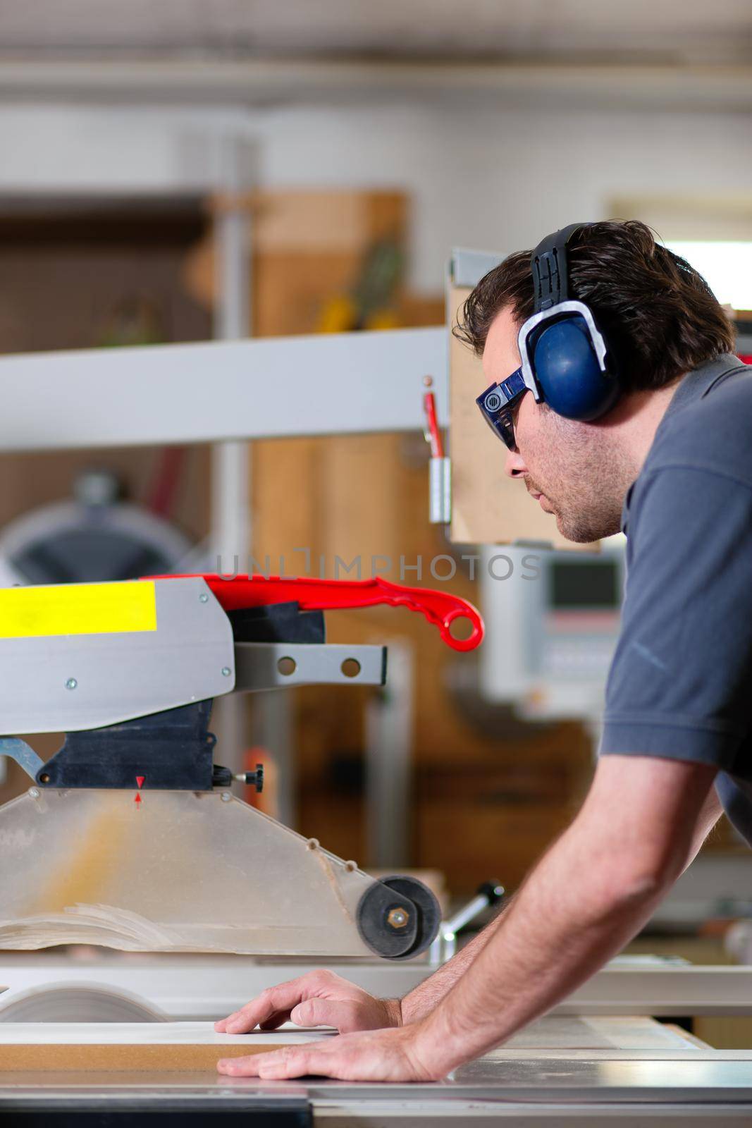 Carpenter working on an electric buzz saw cutting some boards, he is wearing safety glasses and hearing protection to make things safe