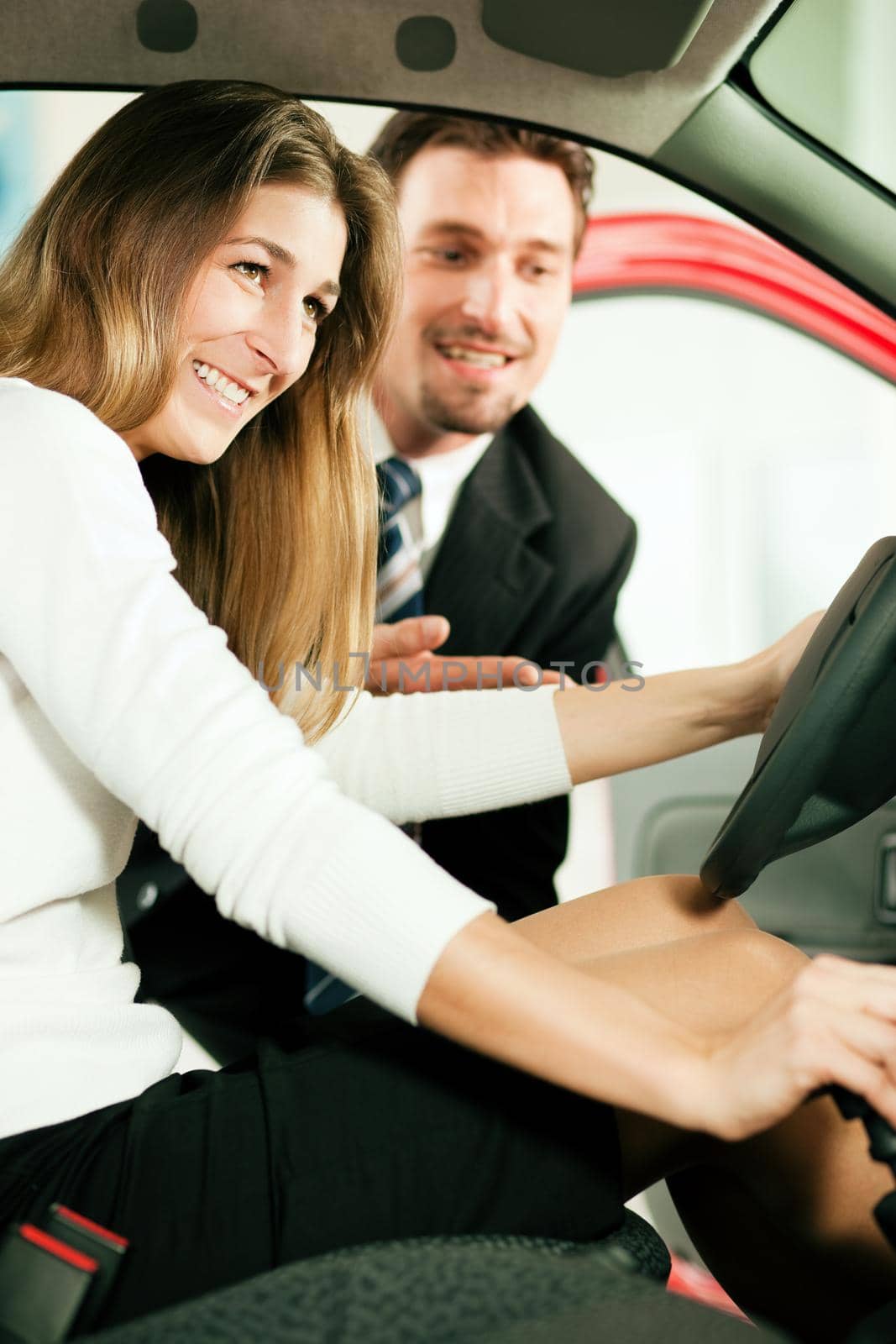 Woman buying a car in dealership sitting in her new auto, the salesman talking to her in the background