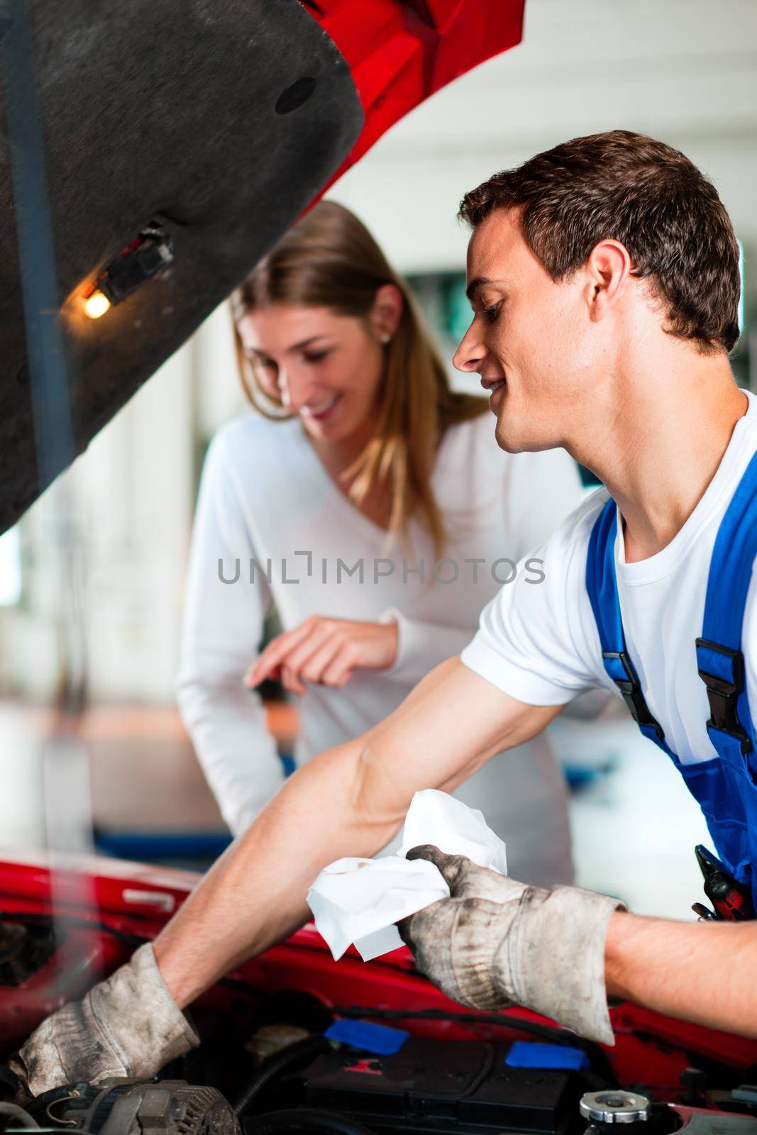 Woman talking to car mechanic in repair shop by Kzenon