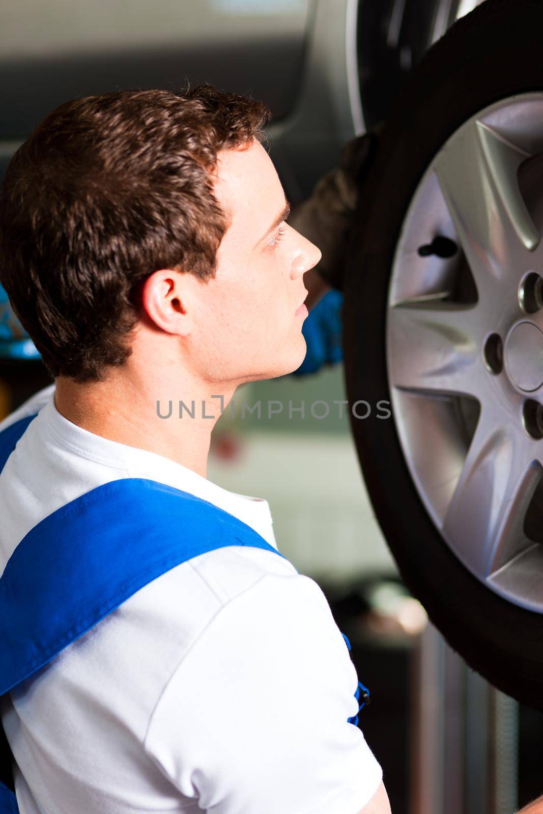 Car mechanic in workshop changing tire by Kzenon