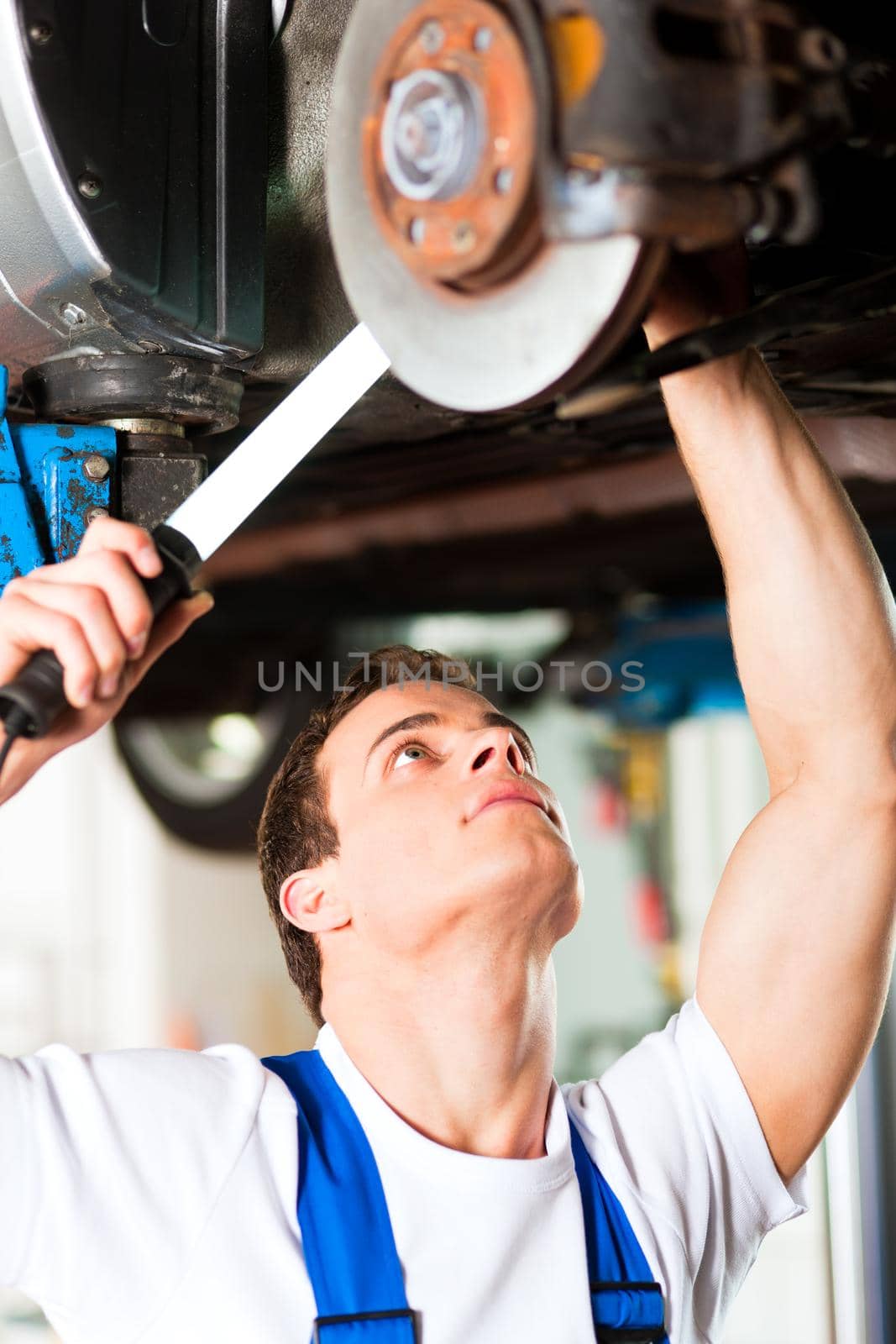 Auto mechanic in his workshop looking under a car on a hoist