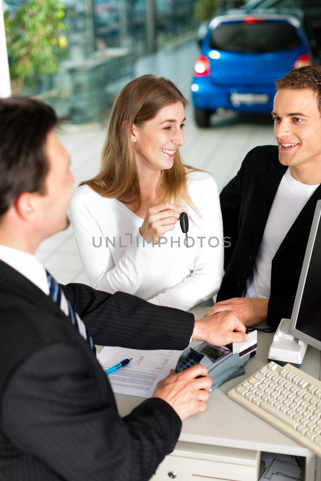 Sales situation in a car dealership, the young couple buys a new car from an agent and pays with credit card