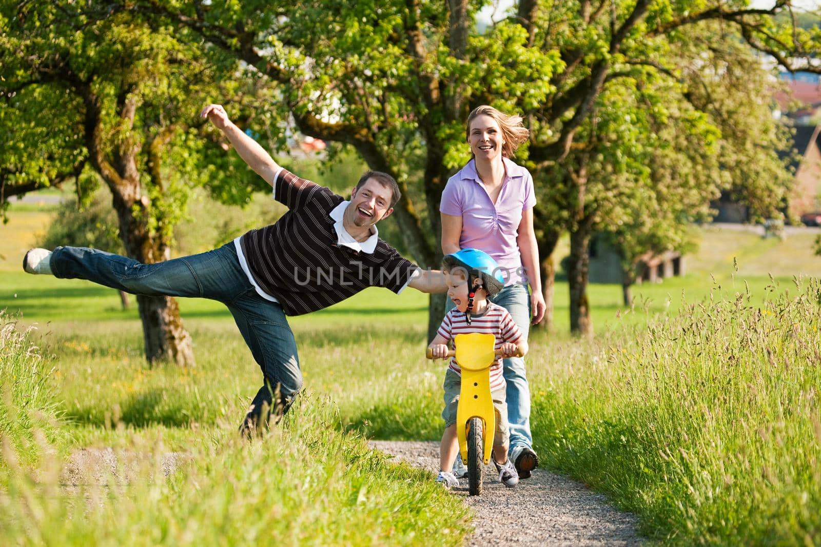 Family having a walk outdoors in summer, their little son using a training bike, unspoiled nature