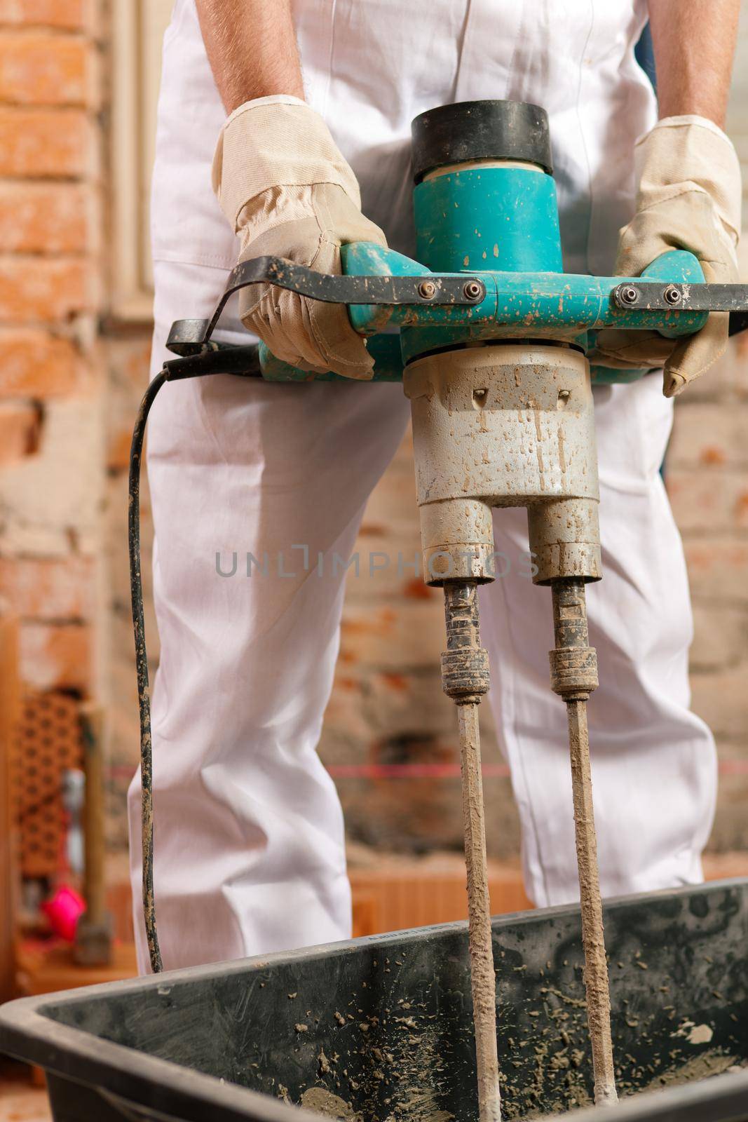 Construction worker mixing concrete or grout with a hand mixer