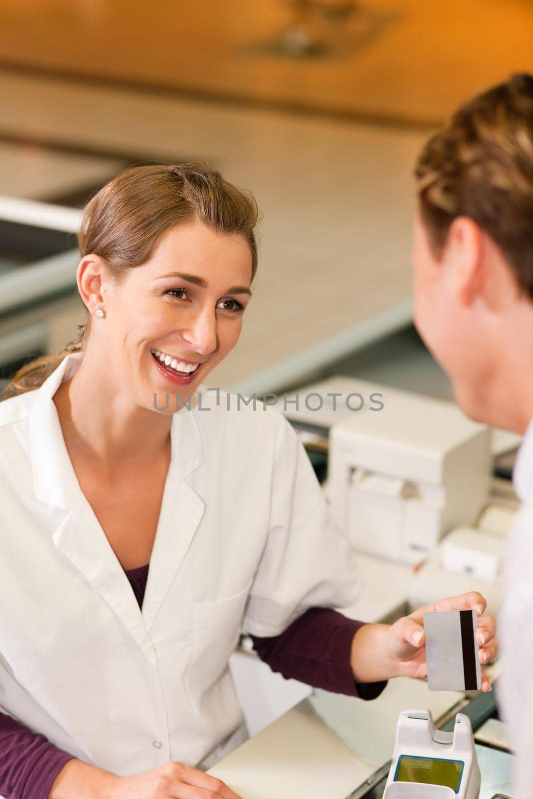 Male customer in supermarket handing his credit card to cashier at the checkout desk in order to pay