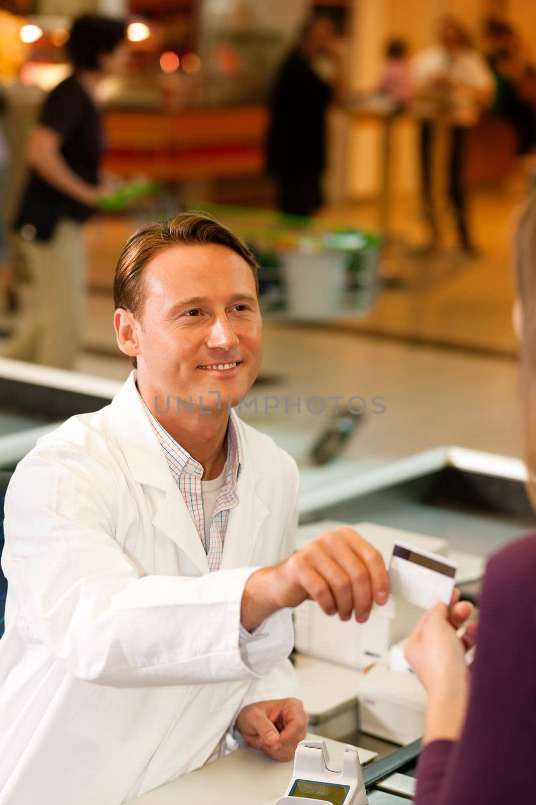 Female customer in supermarket handing her credit card to cashier at the checkout desk in order to pay