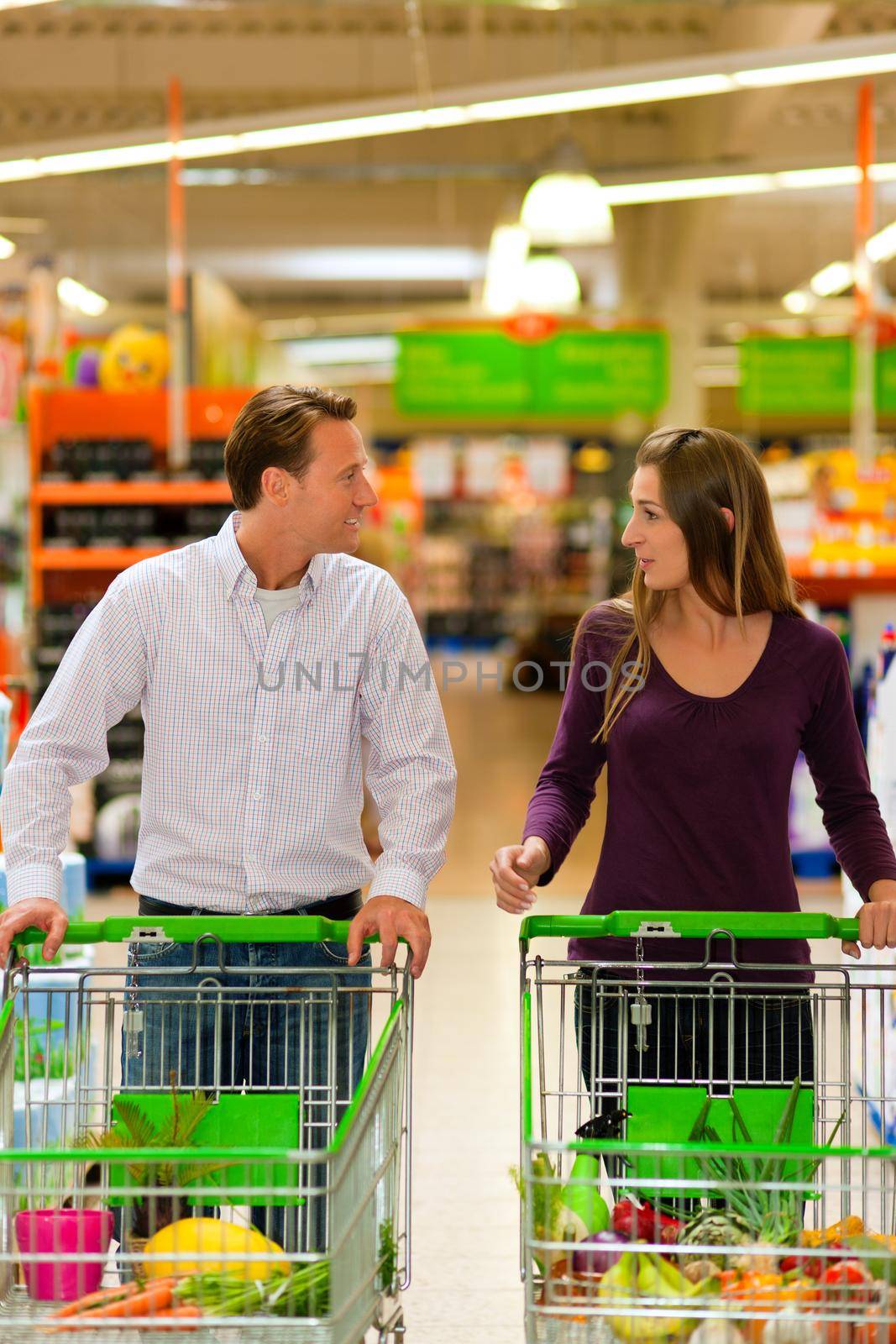 Couple in a supermarket shopping equipped with shopping carts buying groceries; they almost finished