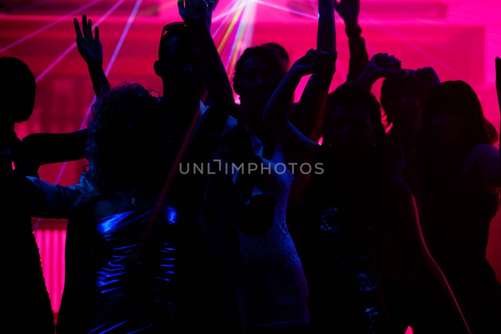 Silhouettes of dancing people having a celebration in a disco club, the light show is sending laser beams through the backlit scene