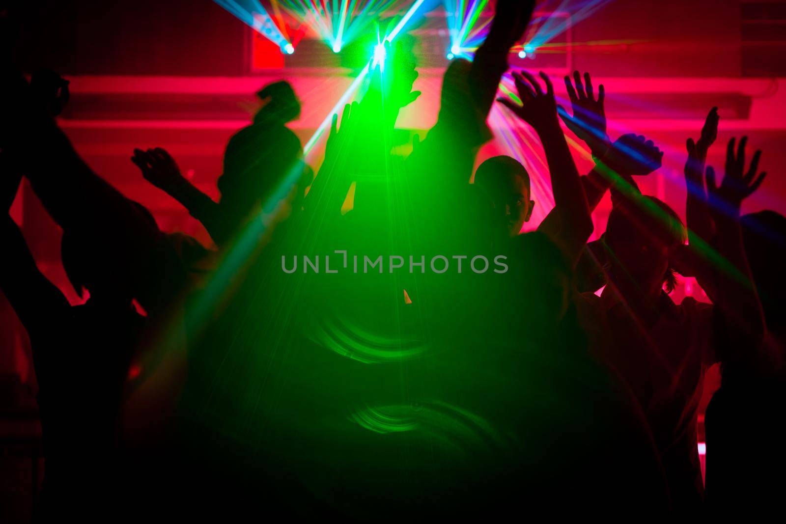 Silhouettes of dancing people having a celebration in a disco club, the light show is sending laser beams through the backlit scene