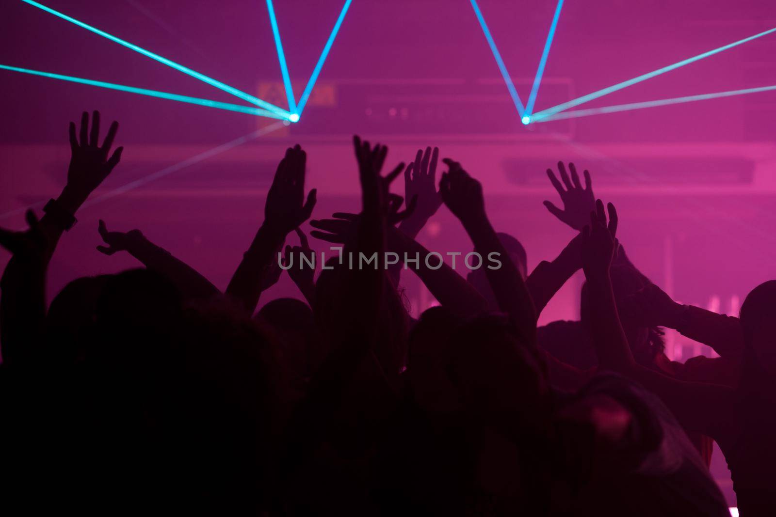 Silhouettes of dancing people having a celebration in a disco club, the light show is sending laser beams through the backlit scene