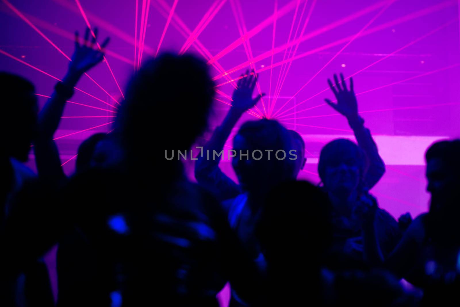 Silhouettes of dancing people having a celebration in a disco club, the light show is sending laser beams through the backlit scene, FOCUS IN ON THE BEAMS!