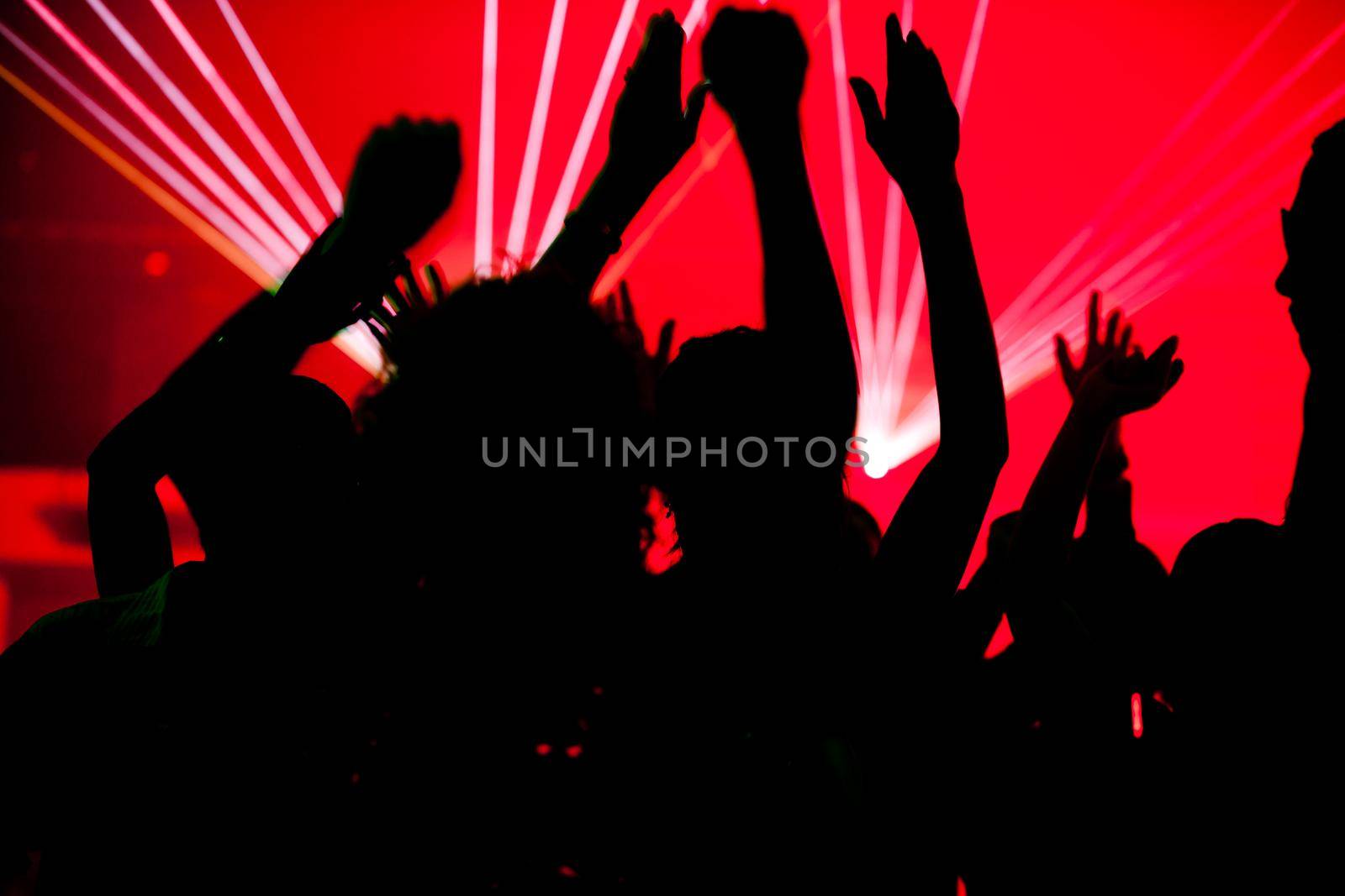 Silhouettes of dancing people having a celebration in a disco club, the light show is sending laser beams through the backlit scen