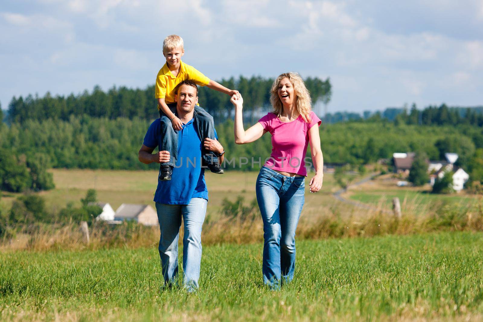 Young family having a walk in the sun over the meadow on a bright summer day