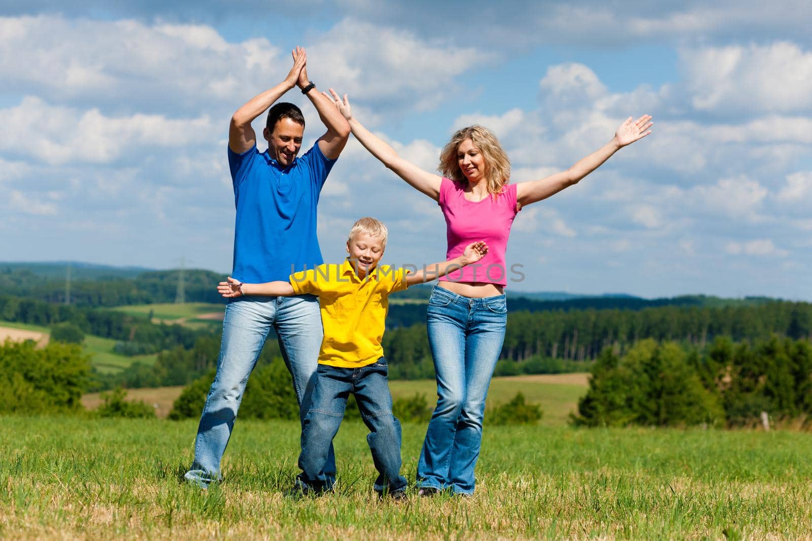 Young family having a walk in the sun over the meadow on a bright summer day and making jokes