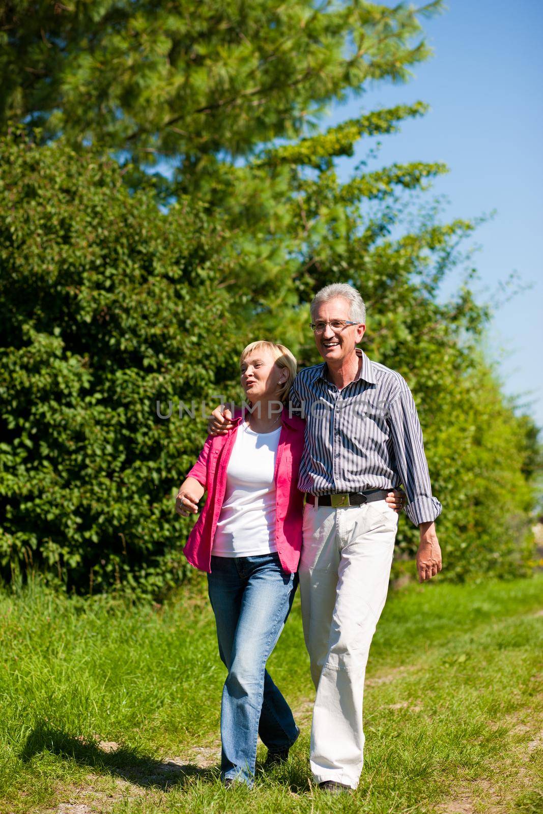 Visibly happy mature or senior couple outdoors arm in arm having a walk