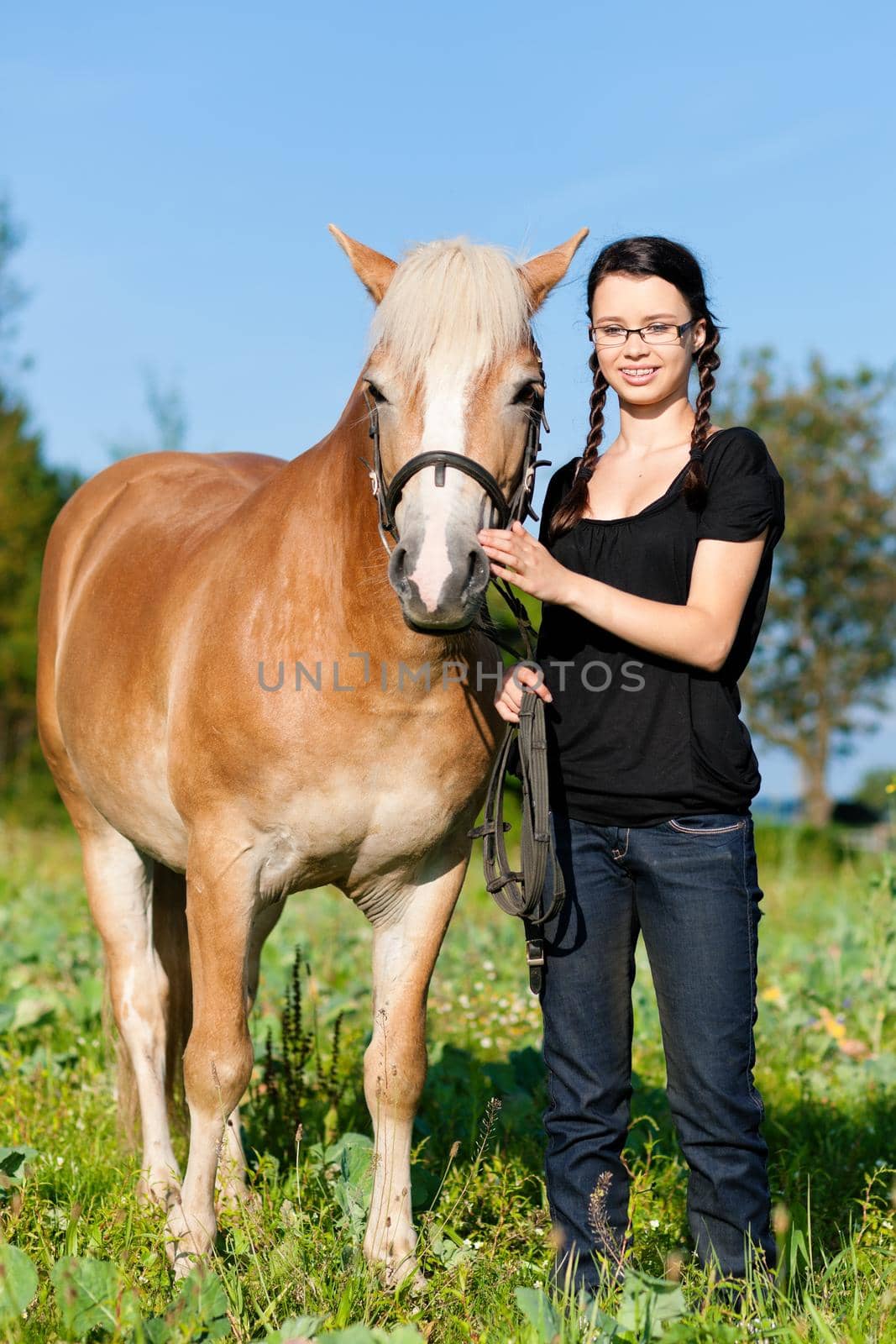 Teenage girl standing on a meadow in summer with her horse