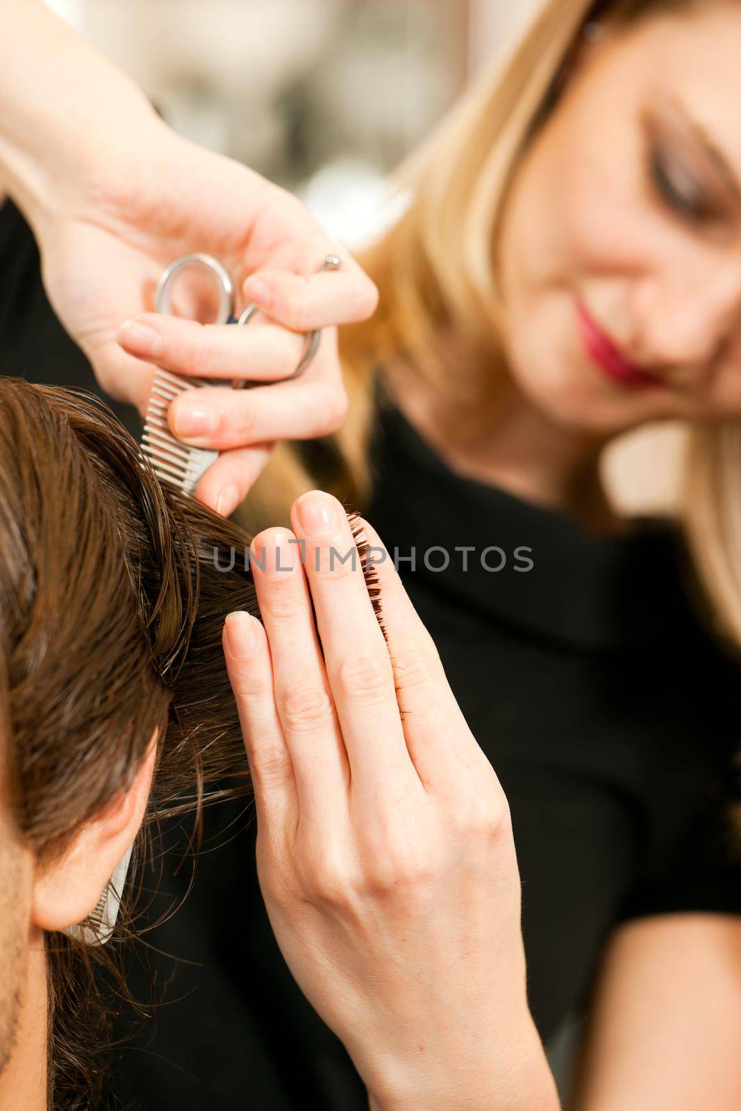 Man at the hairdresser, she is cutting - close-up with selective focus on her hand