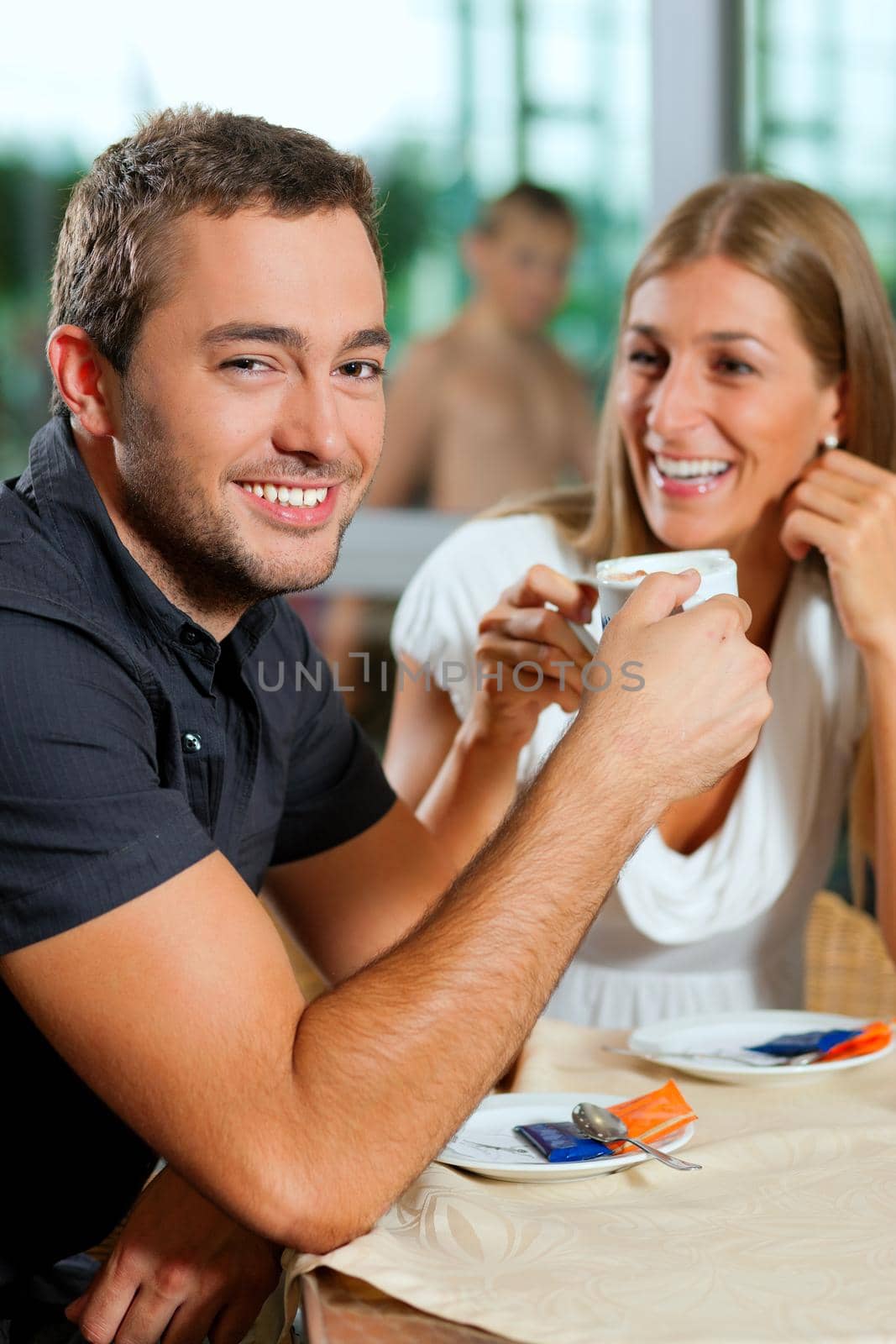 Young couple - man and woman - drinking coffee in a cafe in front of a glass facade