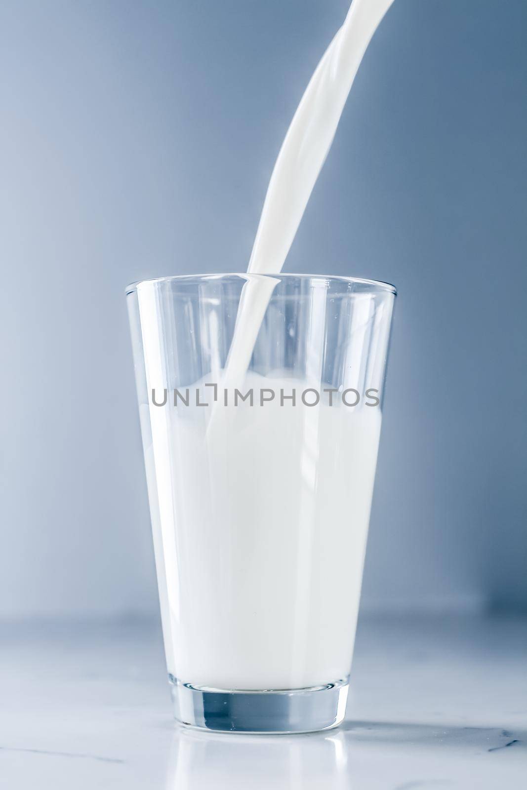 Dairy, healthy nutrition and breakfast concept - World Milk Day, pouring into glass on marble table