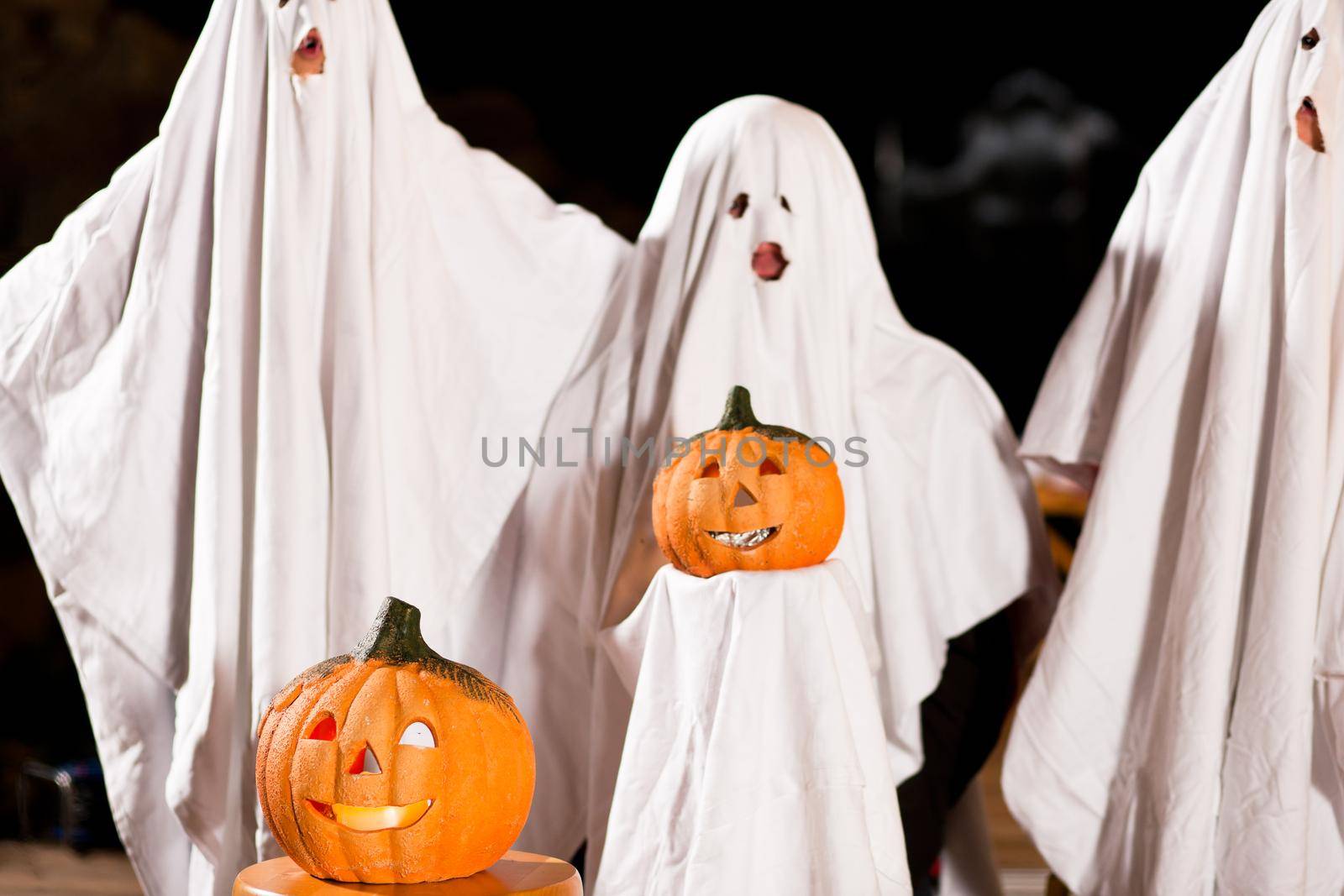 Three very, very scary spooks - kids dressed as ghosts - on Halloween or for carnival or a costume party, FOCUS IS ON PUMPKIN