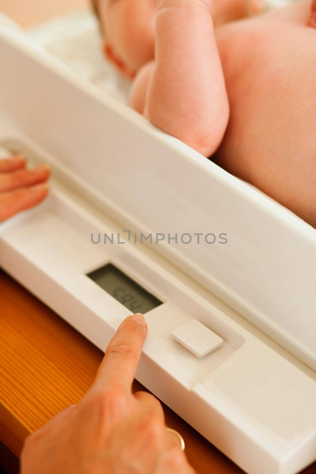 Baby on a weight scale, her mother or a doctor is checking health and development of the newborn