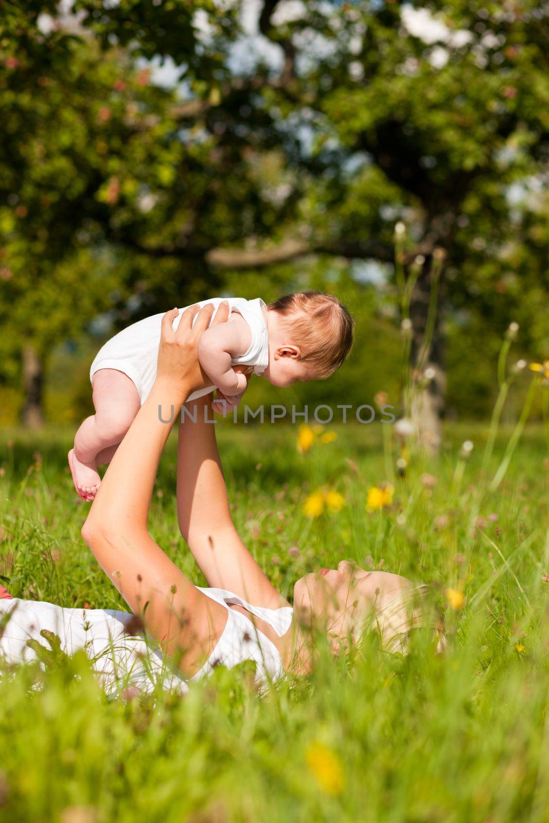 Mother playing with her baby on a great sunny day in a meadow with lots of green grass and wild flowers