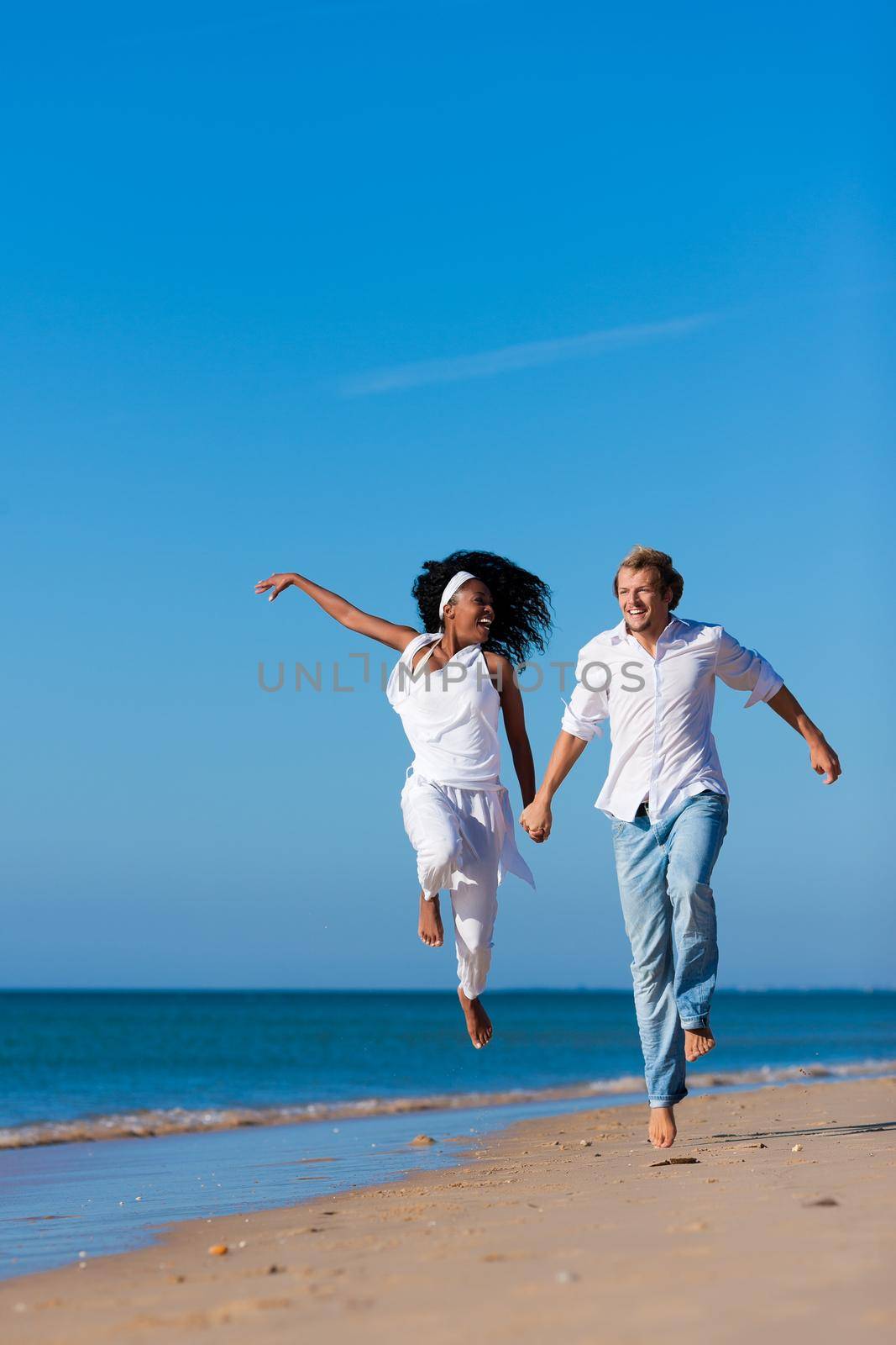 Couple - black woman and Caucasian man - walking and running down a beach in their vacation