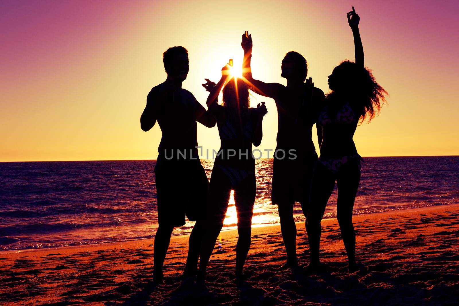 People (two couples) on the beach having a party, drinking and having a lot of fun in the sunset (only silhouette of people to be seen, people having bottles in their hands with the sun shining through)