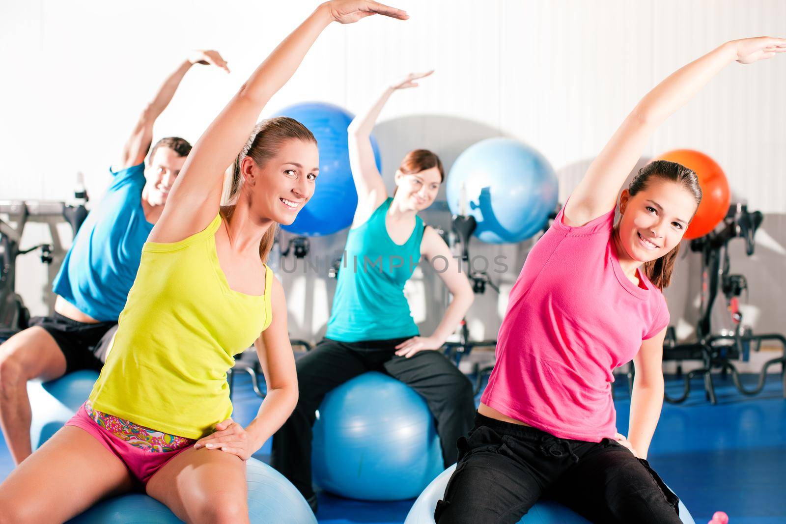 Four people - man and women - in the gym doing gymnastics on an exercise ball