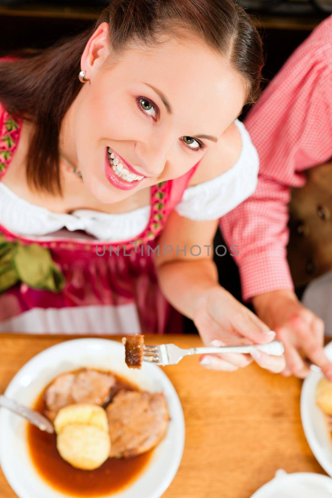 Inn or pub in Bavaria - couple in traditional Tracht drinking beer and eating roast pork with dumplings