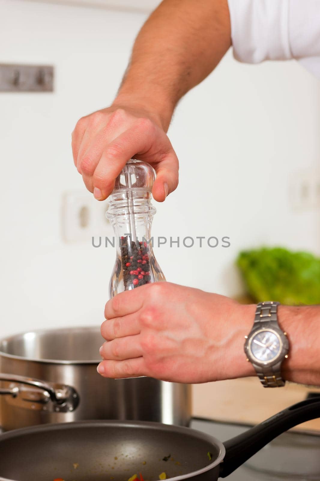 Man in the kitchen - only hands to be seen - is adding spices to food
