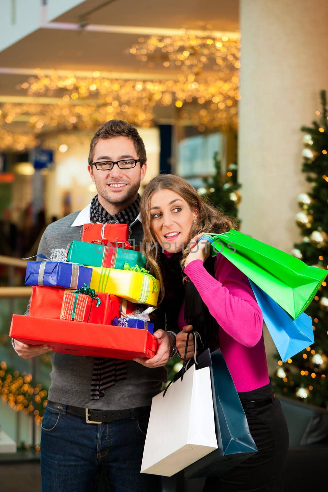 Couple - man and woman - with Christmas presents, gifts and shopping bags - in a mall in front of a Christmas tree