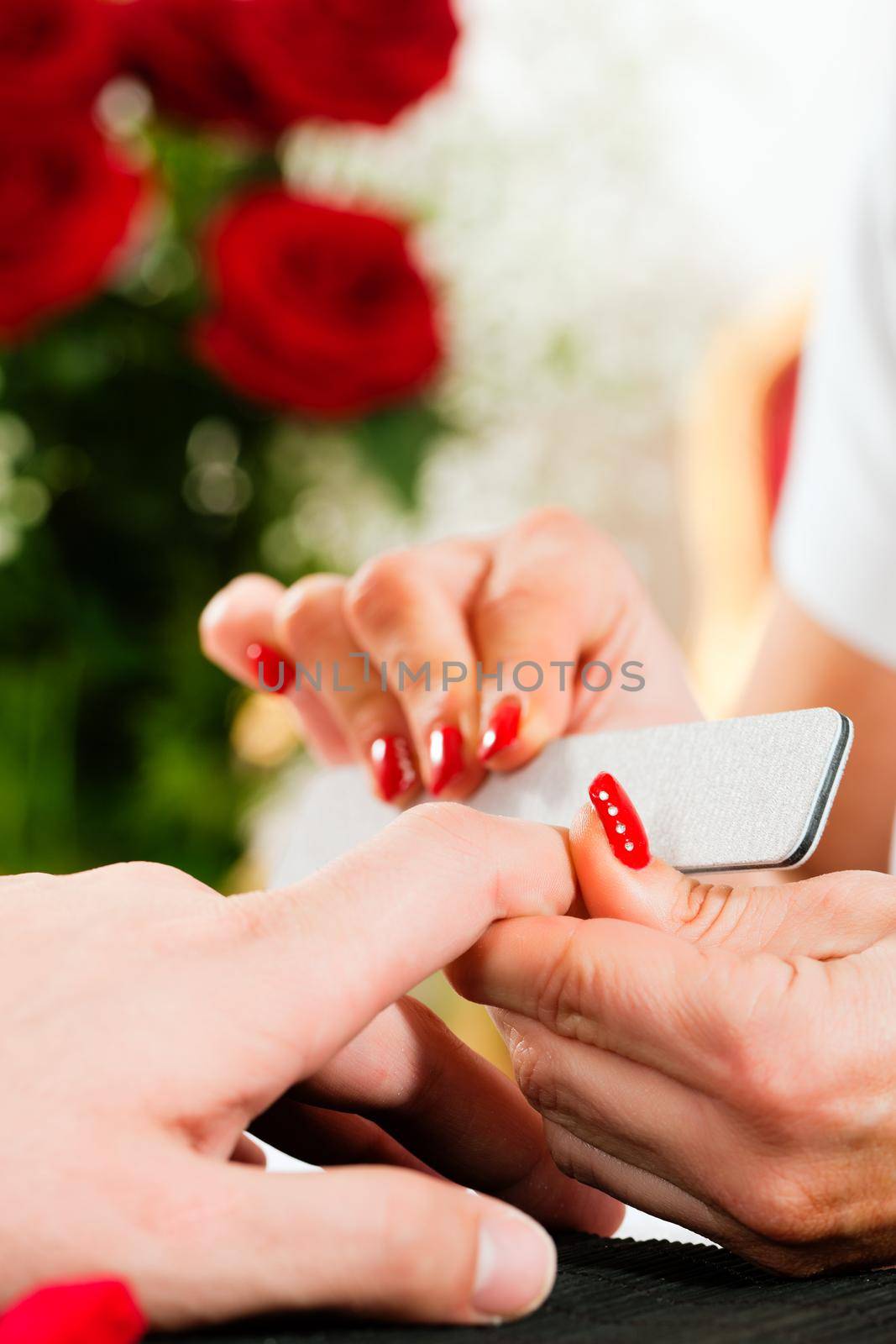 Man in a nail salon receiving a manicure by a beautician, lots of roses in the background