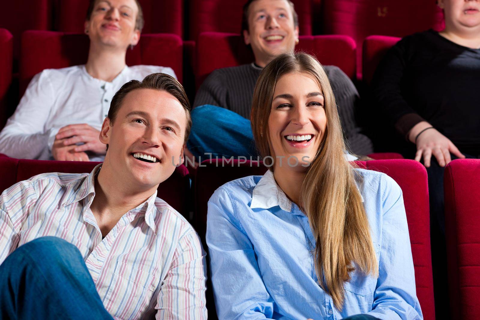 Couple and other people, probably friends, in cinema watching a movie, it seems to be a funny movie