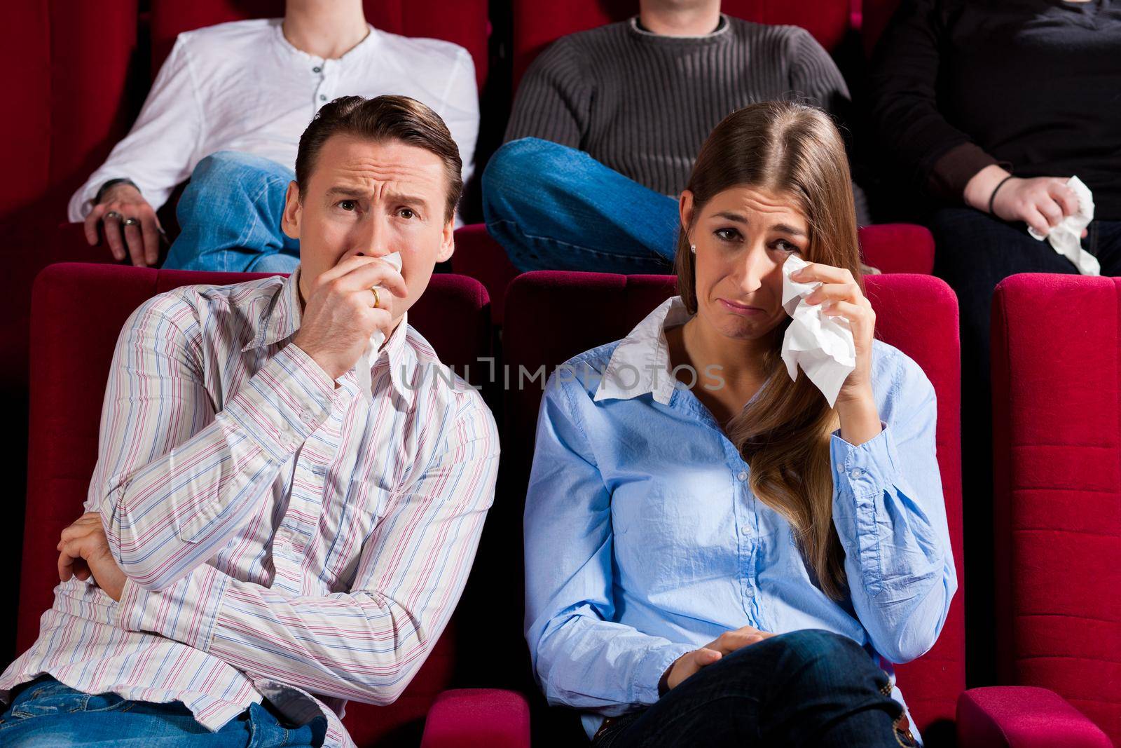 Couple and other people, probably friends, in cinema watching a movie, it seems to be a sad movie