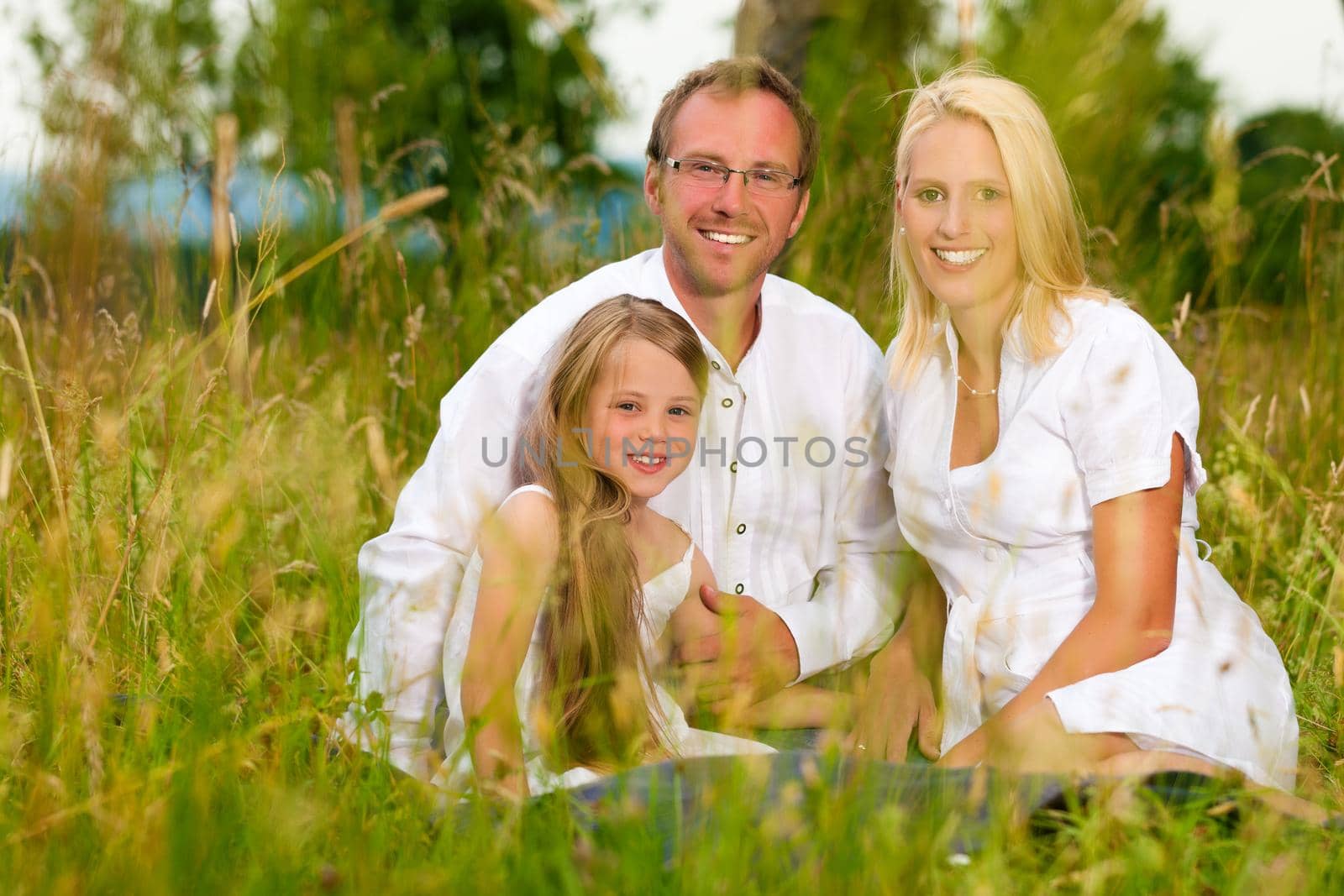 Happy family sitting in meadow by Kzenon
