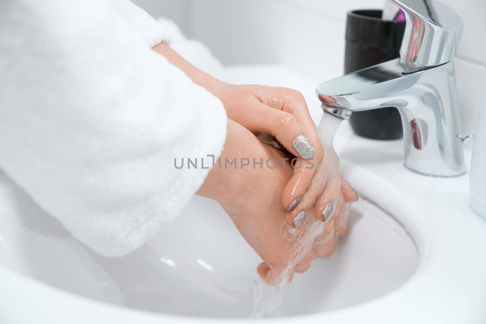 Close up of young woman with trendy manicure washing hands at home in bathroom. Concept of process care for hands and body with special creams and soaps.