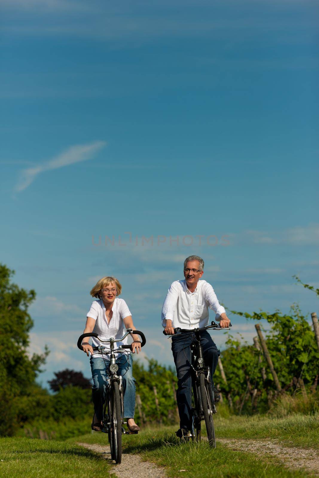 Happy mature couple - senior people (man and woman) already retired - cycling in summer in nature