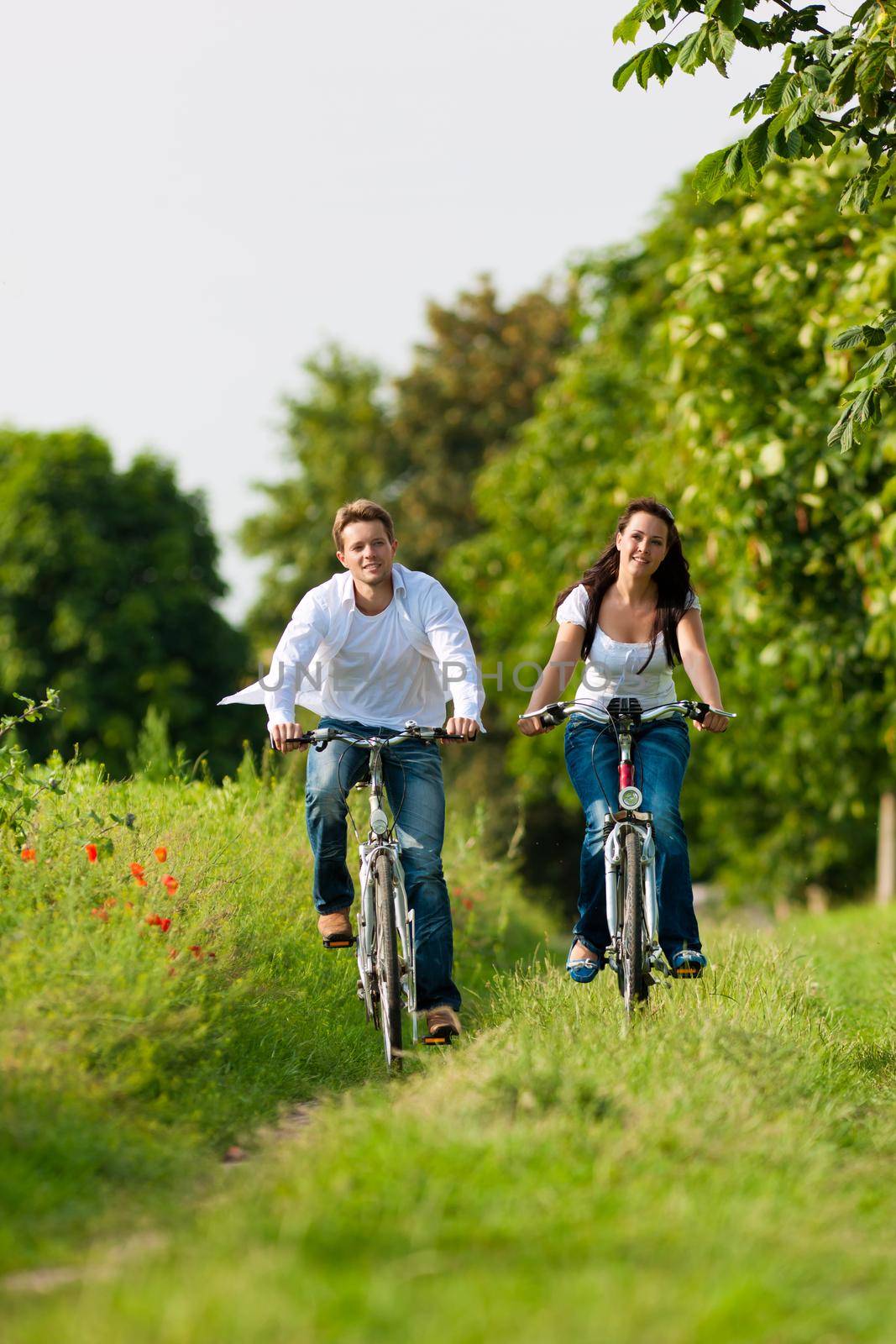 Happy young couple - man and woman - cycling in summer in nature