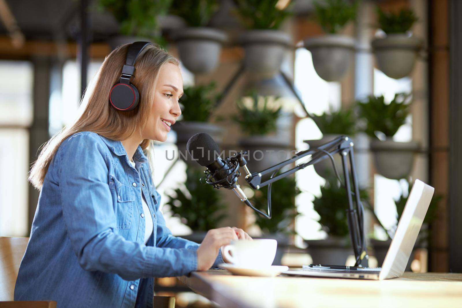 Side view of smiling young beautiful woman working in laptop with headphone in cafe with tasty coffee. Concept of process communication in live broadcast with people.