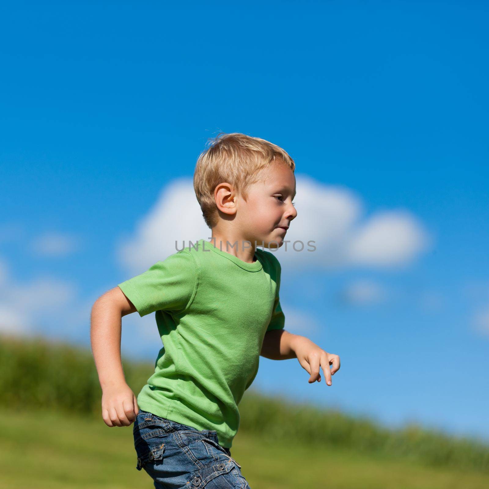 Little boy running down a meadow in a beautiful landscape in summer