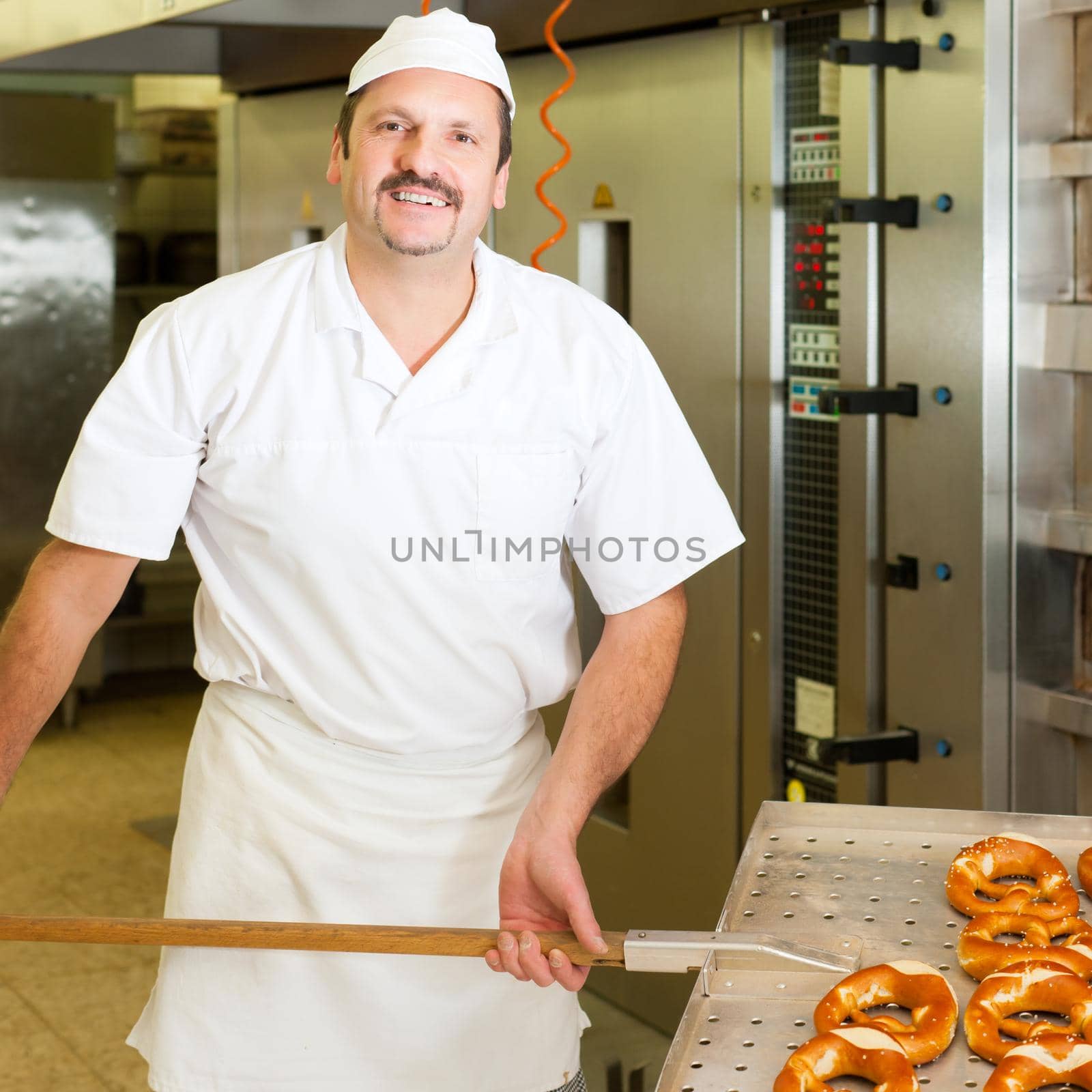 baker standing in his bakery in the morning and is baking bread or buns
