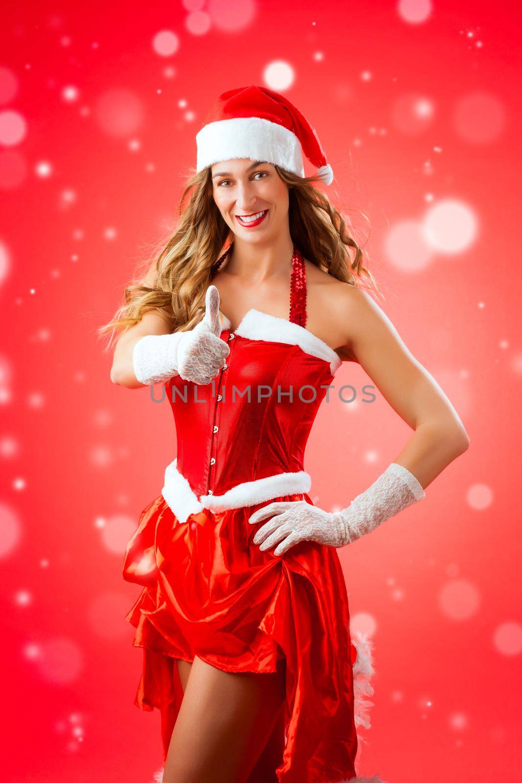 Attractive young woman in Santa Claus costume with thumbs up okay approval snow flakes on isolated red background Xmas celebration festive winter smiling happy