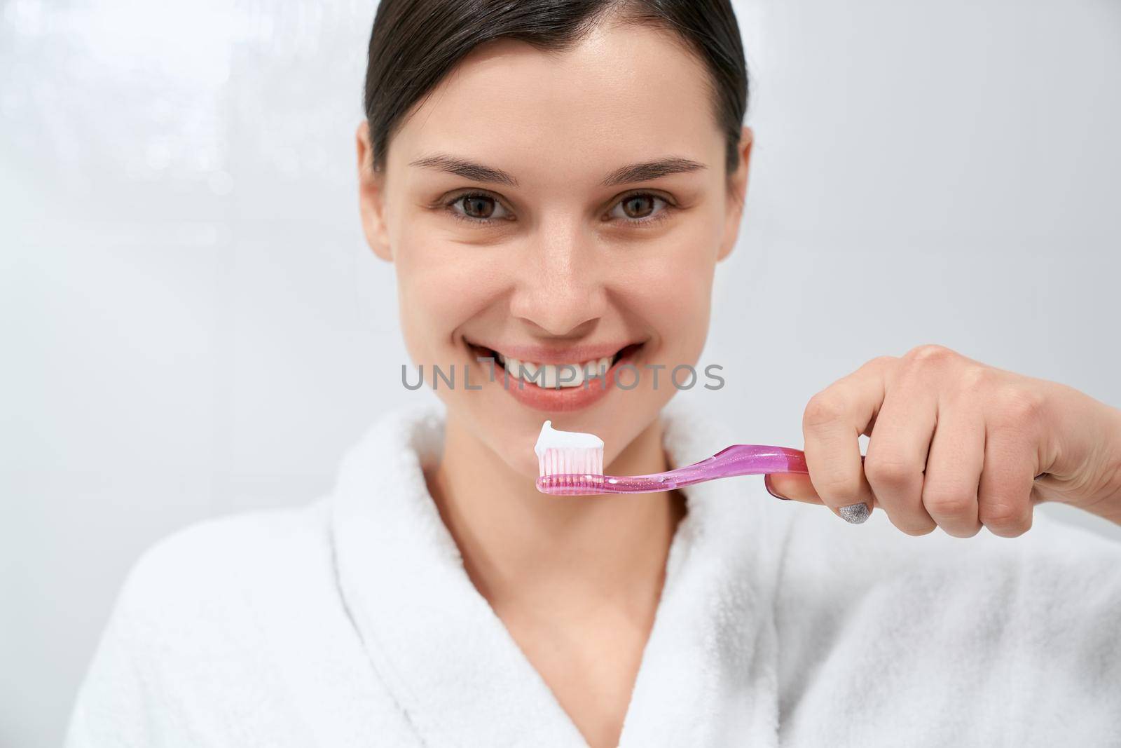 Woman in white robe after shower holding toothbrush. by SerhiiBobyk