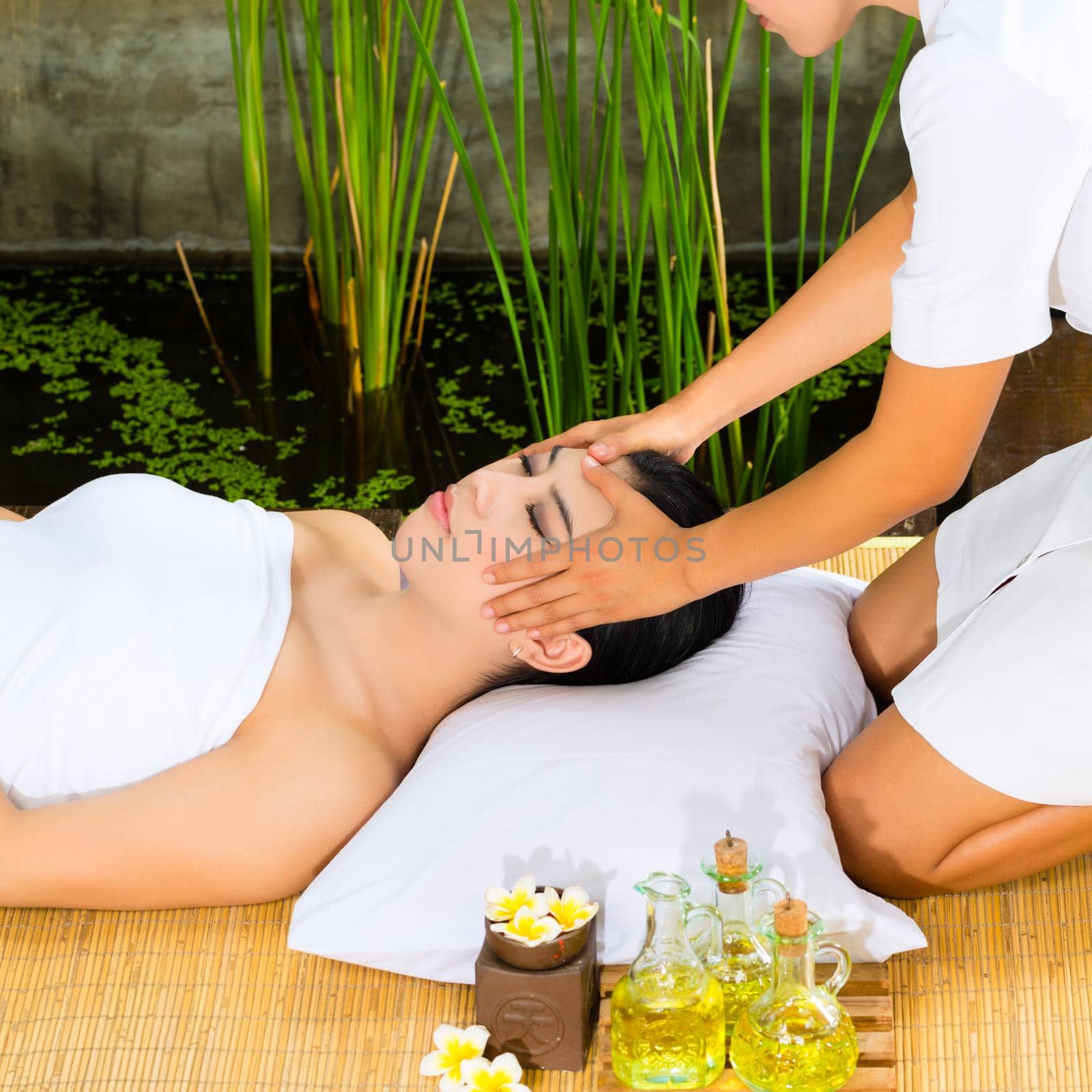 Beautiful Asian woman having a wellness Head massage in a tropical setting and feeling visibly good about it