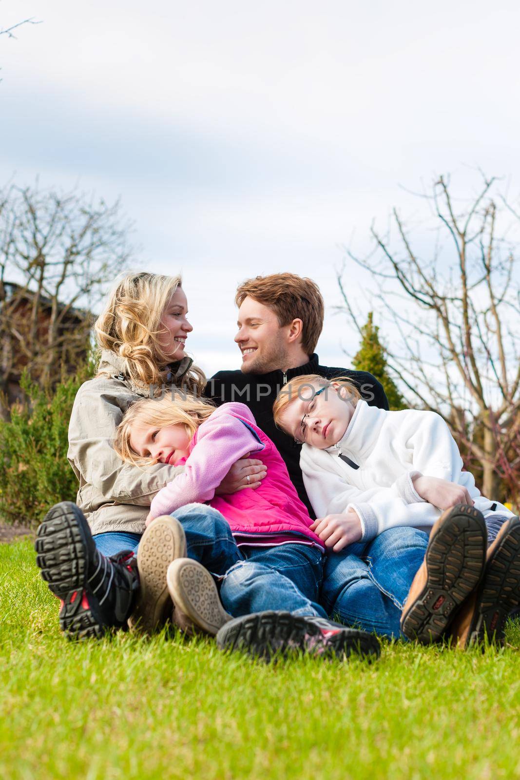 Family sitting together on a meadow in spring by Kzenon