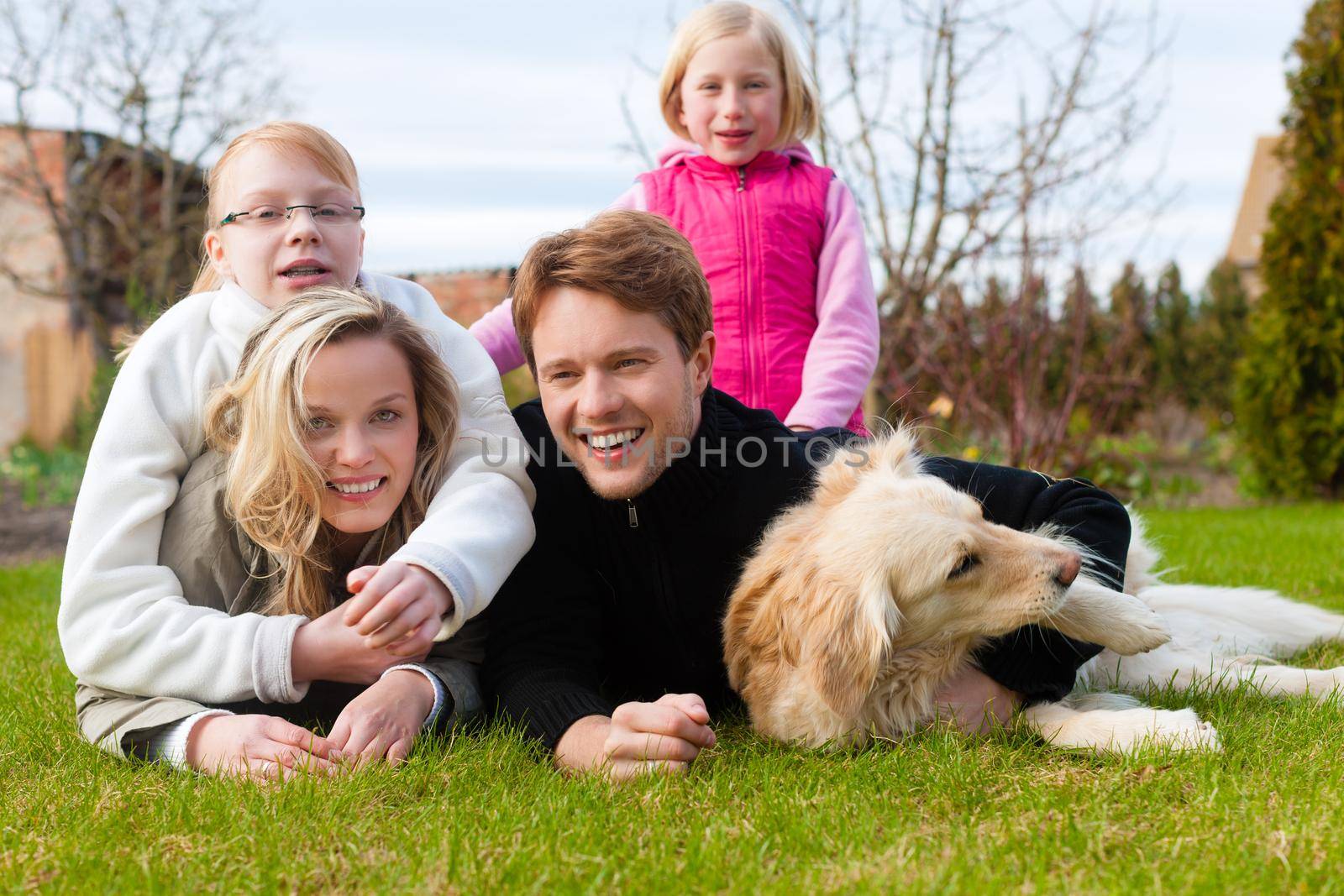 Family, father, mother and daughters, sitting together with their dog on a meadow, they are laughing and have fun